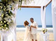 A couple getting married under a wooden trellis on the beach.