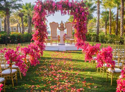 A cultural wedding set up outside with pink flowers and a flower arch on the alter.