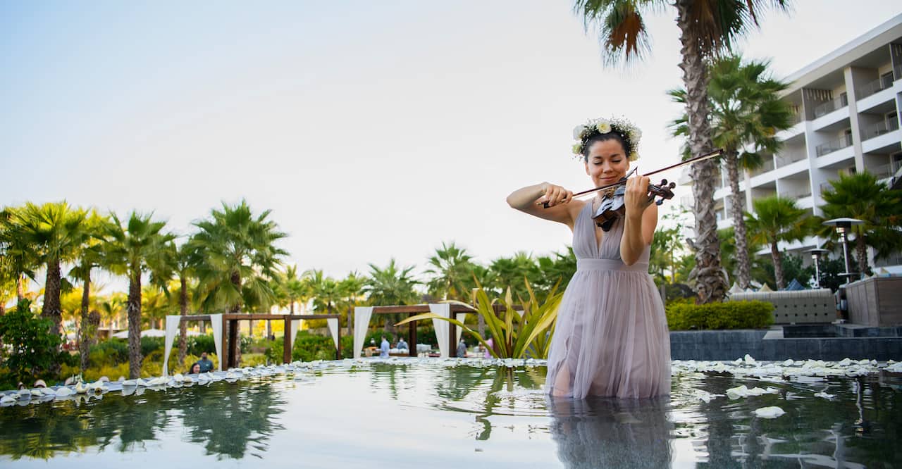 A person standing within a body of water with flower petals playing violin.