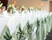 Wedding Reception Top Table With Place Settings, Flowers, Wine Glasses, and Chairs With Green Bows