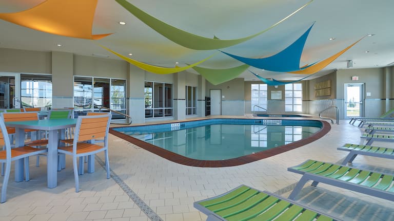 Tables, chaises, chaises longues et fenêtres avec vue sur la piscine intérieure et décoration colorée du plafond