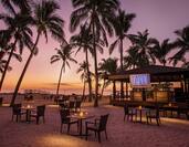 Sunset View of Candlelit Tables and Chairs Surrounded by Sand and Palm Trees at Tavu Grill