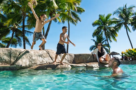 Family playing in outdoor hotel pool surrounded by tropical palm trees