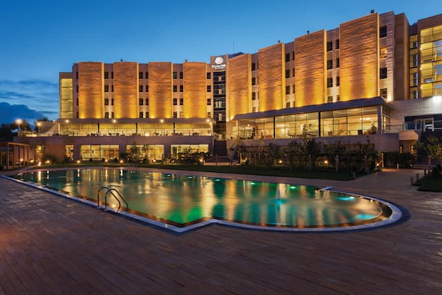 Illuminated Swimming Pool, Hotel Exterior, Signage, and Landscaping at Night