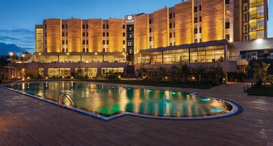 Illuminated Swimming Pool, Hotel Exterior, Signage, and Landscaping at Night