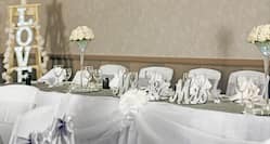 Detailed View of Place Settings and Flowers on Head Table With White Linens Set Up For Wedding Reception With Illuminated "Love" Light in the background of Oxford Suite