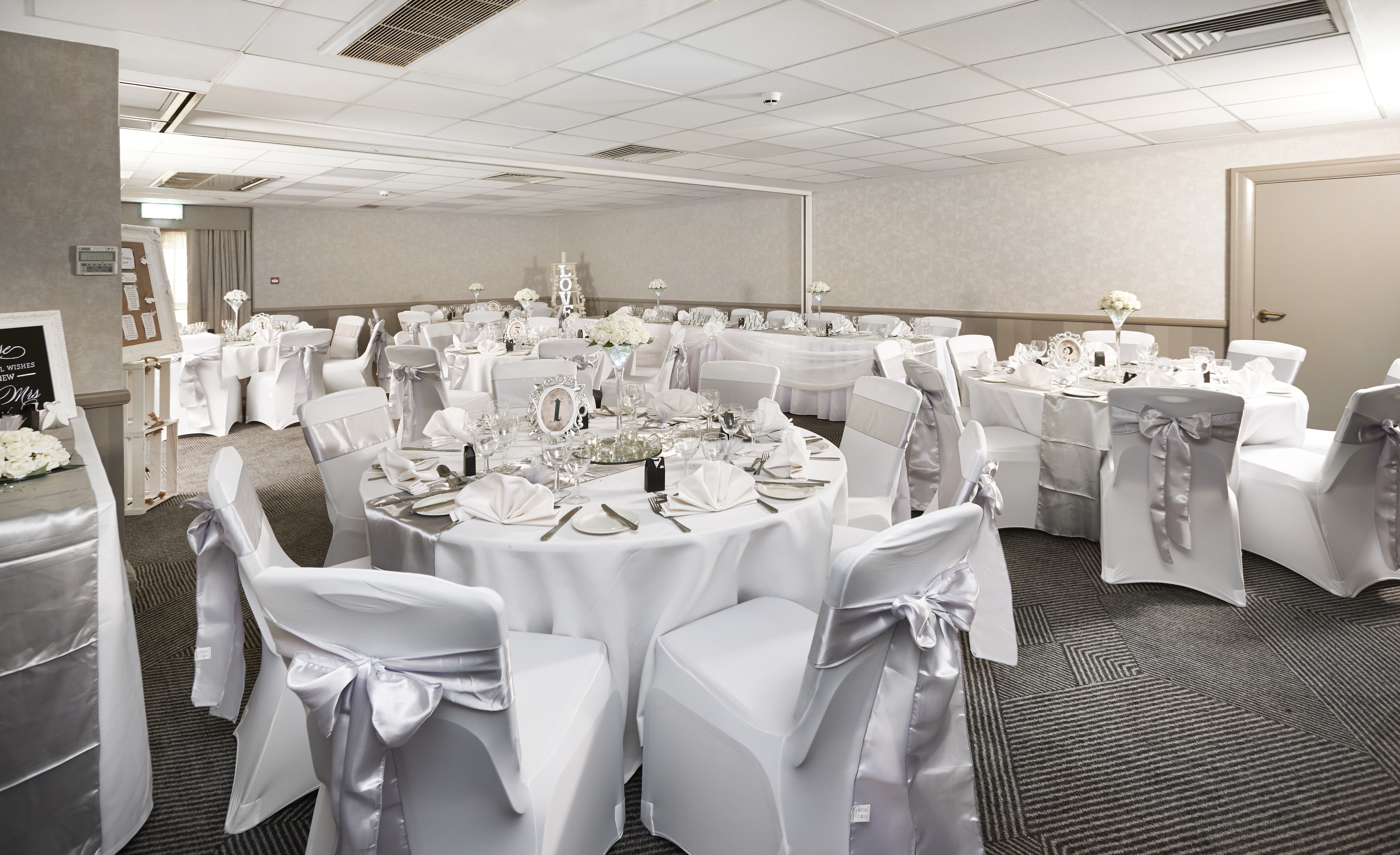Place Settings, Wine Glasses, Photo Frame and Napkins on Round Tables With White Linens Decorated for Wedding Reception in Oxford Suite