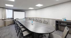 Angled View of Window With Sheer Drapes, Presentation Screen, Beverage Station, and Seating For 16 At Boardroom Table With Water Bottles and Drinking Glasses in Hermitage Suite