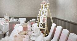 Detailed View of White Chairs With Pink Bows, Place Settings, Wine Glasses on Head Table With White Linens, and Small Ladder in Corner With White Flowers and Illuminated "Love" Light Set Up For Wedding Reception