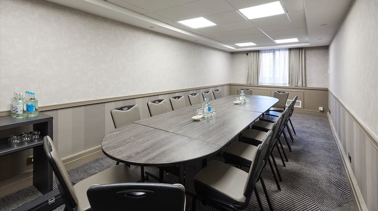  Angled View of Beverage Station, Seating For 16 at Table With Water Bottles and Drinking Glasses, and Window With Sheer Drapes  in Wickham Boardroom