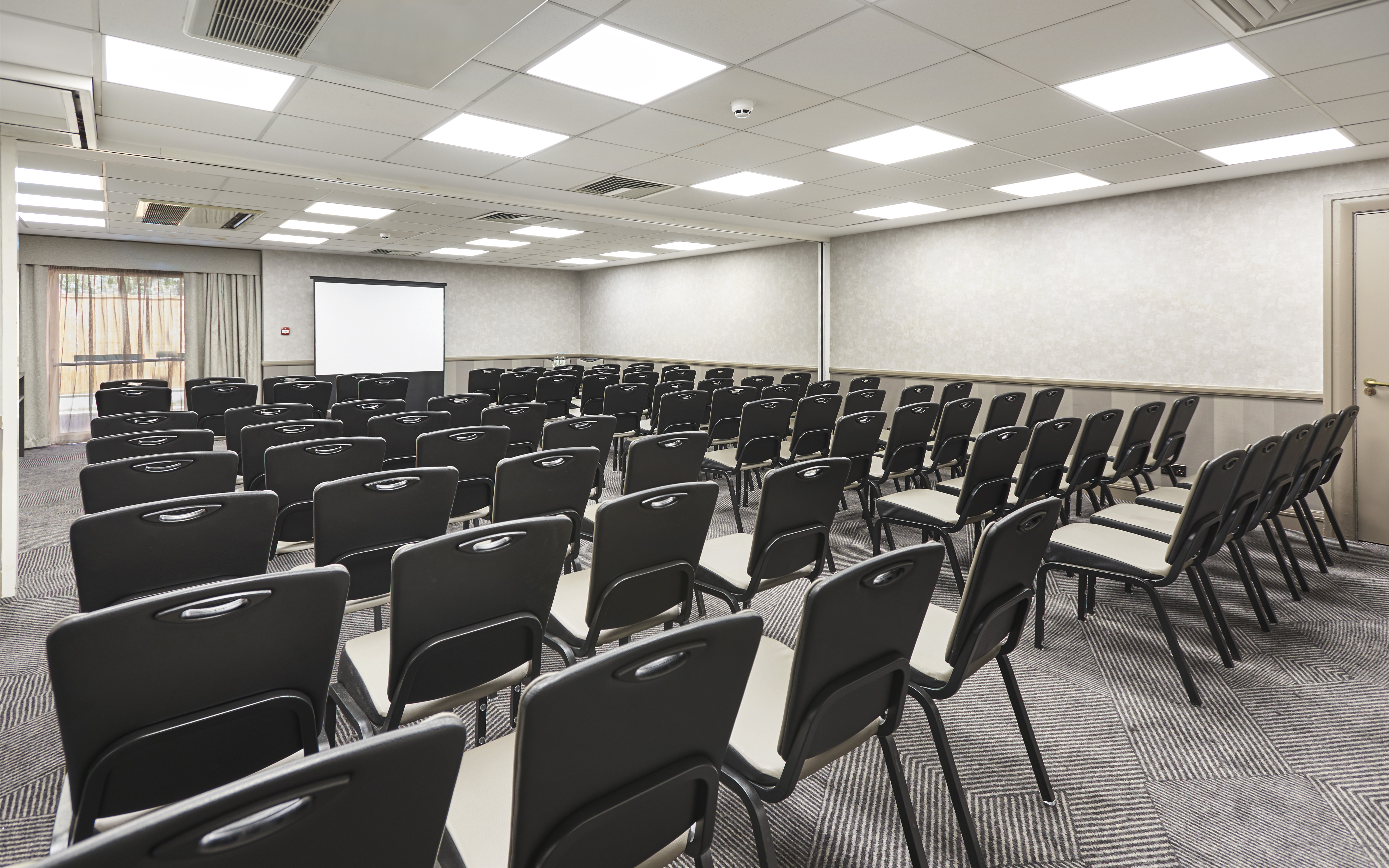 Enbourne Suite Arranged Theater Style With Rows of Chairs Facing Projector Screen and Window With Sheer Drapes