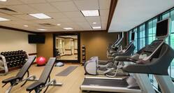 Fitness Center With Cardio Equipment Facing Windows, Weight Benches, Free Weights, TV, Red Exercise Ball, Large Mirrored Wall and Weight Balls