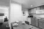 Kitchen With Fridge, Dishwasher, Toaster, Coffee Maker, Sink, and Microwave Over Stovetop,  Seating for Two at Dining Table, and Open Doorway to Bedroom 
