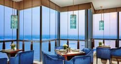 Place Settings and Flowers on Tables With Plush Blue Armchairs by Windows With Sunset View in Executive Lounge