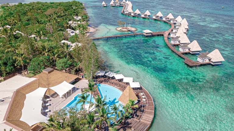 Drone view of resort pool, tropical greenery and ocean guest rooms