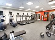 Fitness Center With Free Weights, Weight Bench, Cardio Equipment, Weight Balls, Water Cooler, TV Above Towel Station, Red Exercise Ball, and Large Mirror by Weight Machine