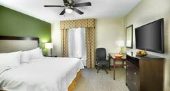 King Bed and Bedside Table With Lamp, Ceiling Fan, Work Desk by Window, and TV in Suite Guest Room