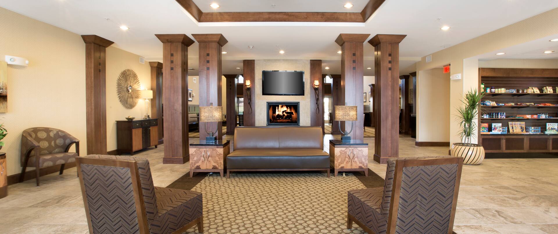 TV Above Fireplace in Lobby Lounge Area With Wood Columns, Soft Seating, Tables, and View of Snack Shop