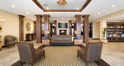 TV Above Fireplace in Lobby Lounge Area With Wood Columns, Soft Seating, Tables, and View of Snack Shop