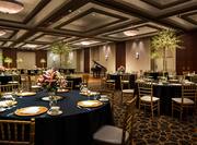 Tables With Flowers and Place Settings on Navy Blue Linens, Chairs, and Grand Piano on Dance Floor in Event Space