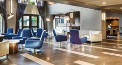 Blue Armchairs, White Sofas, ,Tables, Illuminated Floor Lamps, and Windows With Open Drapes and Outside View in Lobby Lounge