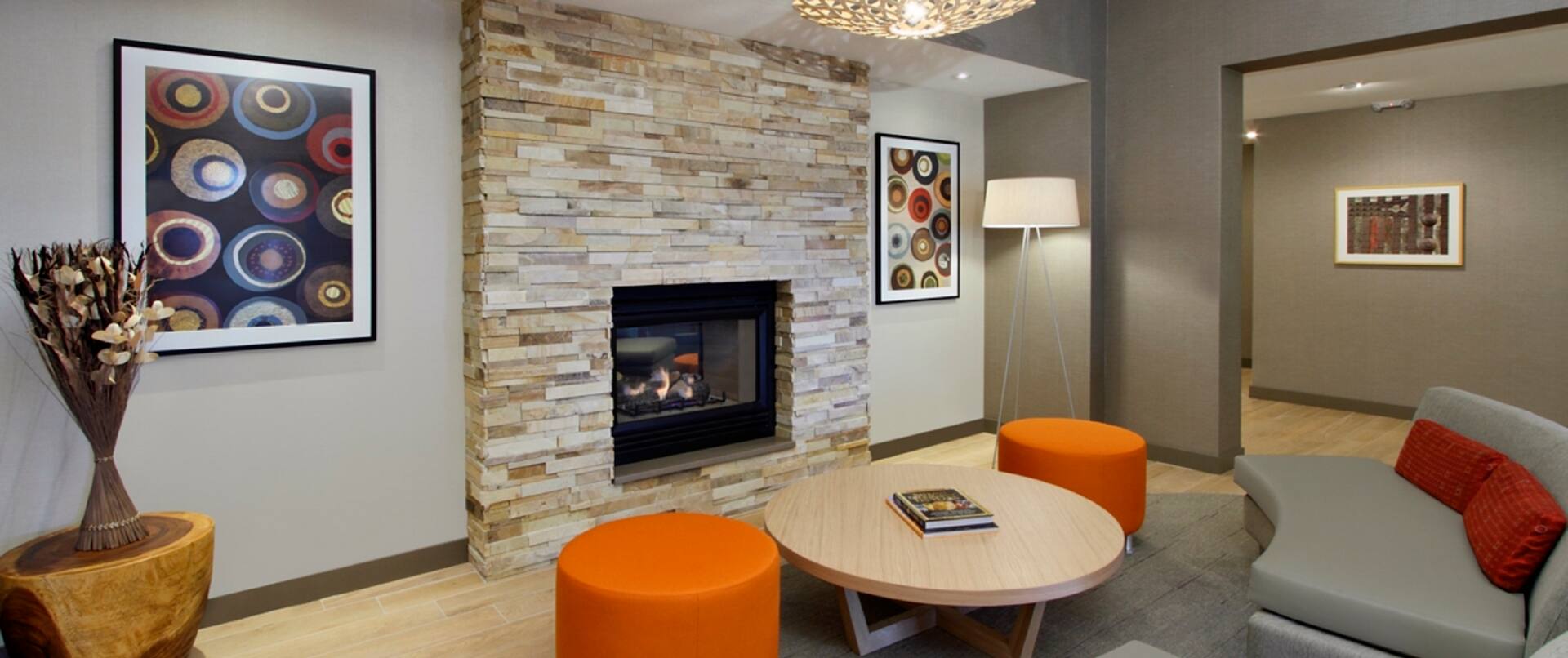 Fireplace Sitting Area With Wall Art, Round Table, Two Orange Ottomans, Floor Lamp and Two Sofas