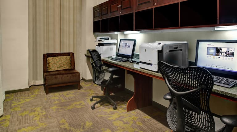 Business center com poltrona estilo lounge chair, janela com cortina leve, duas estações de trabalho de computador, cadeiras ergonômicas, impressora e fax/copiadora