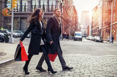Couple Crossing Cobblestone Street Holding Red and Black Shopping Bags