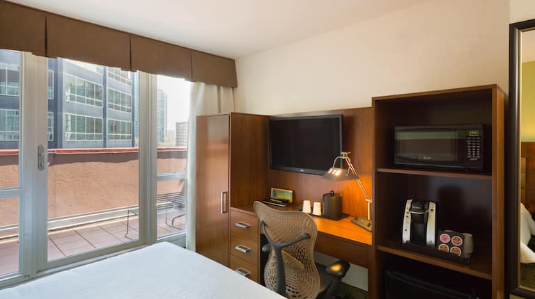 King Bed, Door With Open Drapes to View of Terrace Seating, TV, Work Desk, Hospitality Center With Microwave, Keurig, and Mini Fridge and Full Length Mirror
