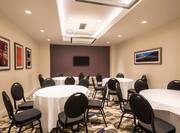 Hudson Meeting Room With Wall Art, Black Chairs Around Round Tables With White Table Cloths, and a TV