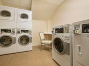 Coin Operated Washing and Drying Machines, Folding Table and Chair in Corner of Guest Laundry Room
