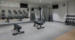 Fitness Center With Weight Benches, Cardio Equipment Reflected in Mirrored Wall, Weight Machine, TVs, Wall Clock, and Free Weights