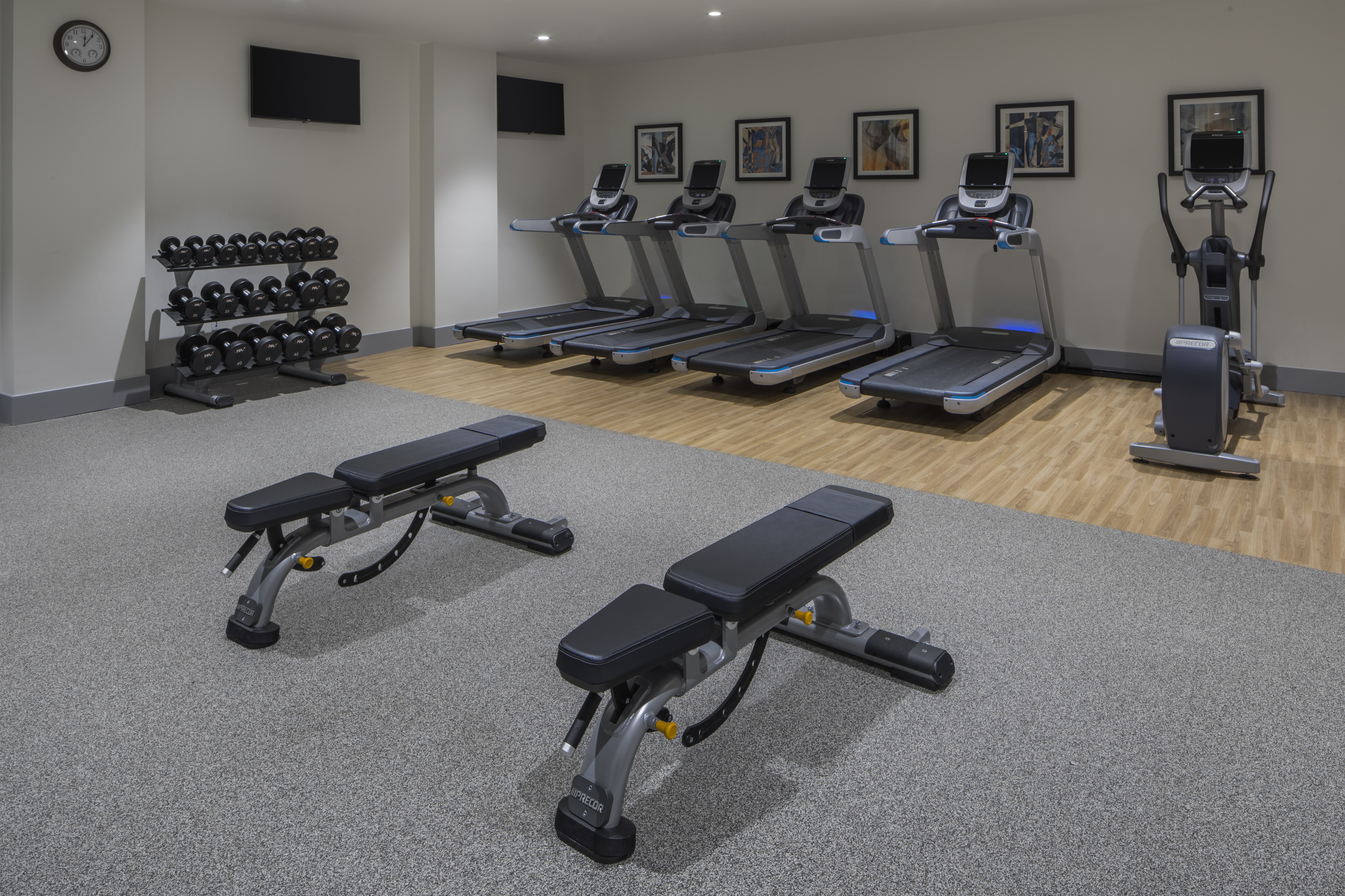 Fitness Center With Weight Benches, Wall Clock, Free Weights, TVs, Cardio Equipment, and Wall Art