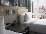 Wall Art Above Two Double Beds, Lamps Above Bedside Table, and Large Window With Open Drapes to View of Downtown City