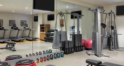 Mirrored Wall WIth Reflection of Cardio Equipment, Wall Art, Towel Station, Free Weights, Aerobic Steppers, Kettle Weights, Benches, and Weight Machine in Fitness Center