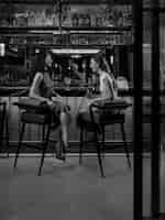 Two women have conversation while sitting at a bar with cocktails