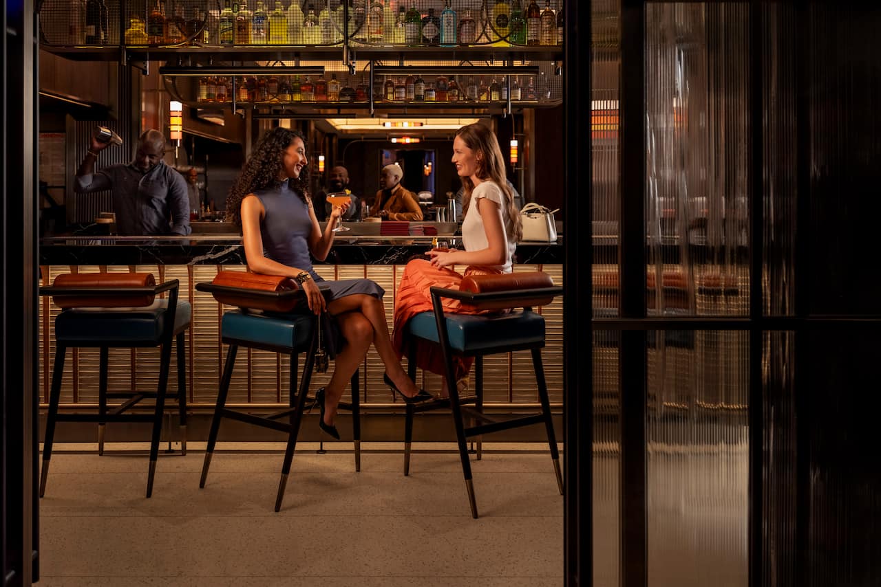 Two women drink cocktails seated at a bar