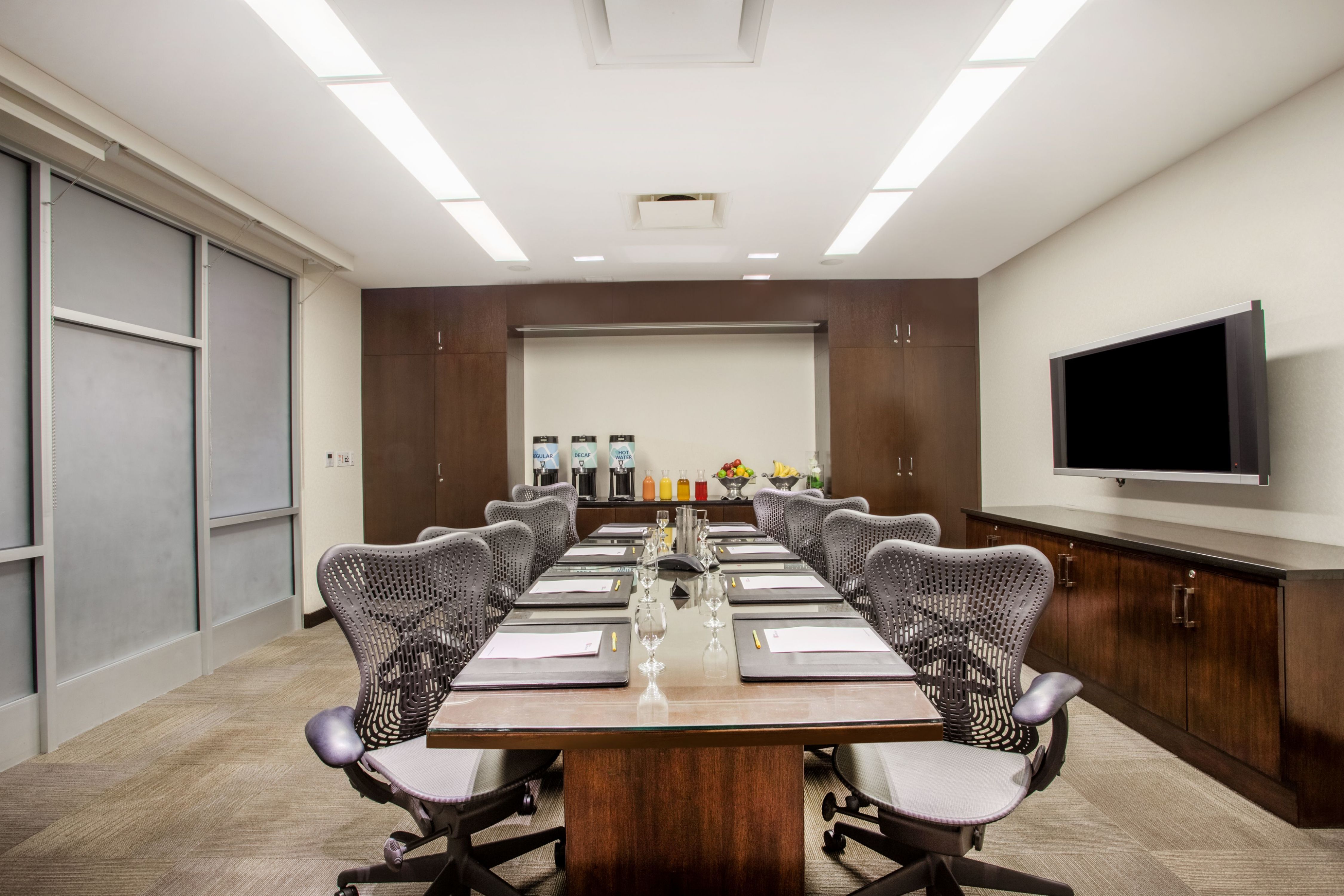 Formaler Boardroom-Tisch mit Notizblöcken, Bürostühlen und an der Wand montiertem HD-Fernseher