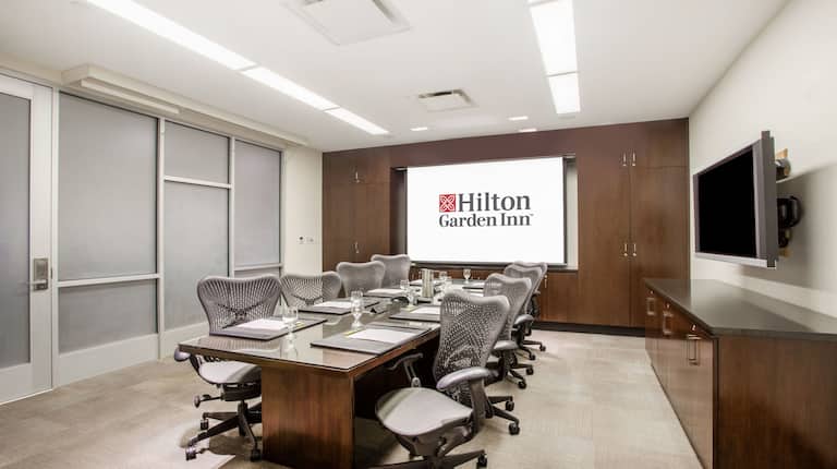 Boardroom with Projector Screen, Table, Notepads, Office Chairs and Wall Mounted HDTV