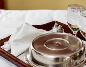 Room Service tray laying on a bed with plate and glasses
