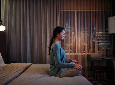 A girl sitting crossed legged on a bed in a dimly-lit room while meditating.