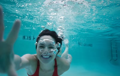 View of Smiling Woman in Red Bathing Suit Swimming Underwater in Pool