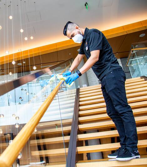 A Hilton employee wearing rubber gloves and a face mask sanitizes a hotel staircase.