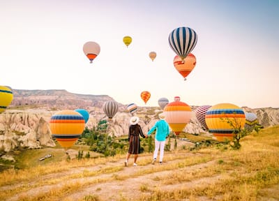 A couple holding hands while watching multiple hot air balloons take off over the Grand Canyon