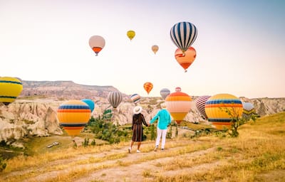 A couple holding hands while watching multiple hot air balloons take off over the Grand Canyon