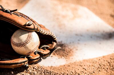 A baseball mit and ball lying on a dirt pitch