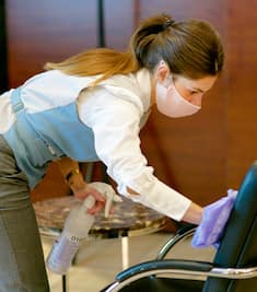 A Hilton Team Member cleaning down a chair with disinfectant spray
