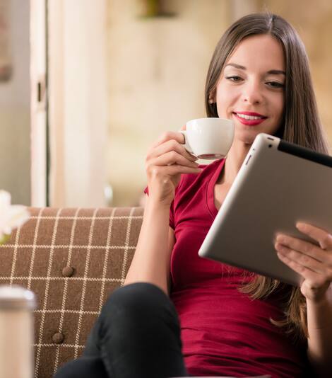 A smiling woman with a tablet computer in one hand and a cup of coffee in another