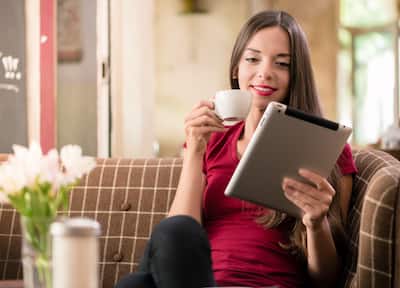 A smiling woman with a tablet computer in one hand and a cup of coffee in another