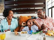 Smiling mother, father and son eating breakfast with large teddy bear